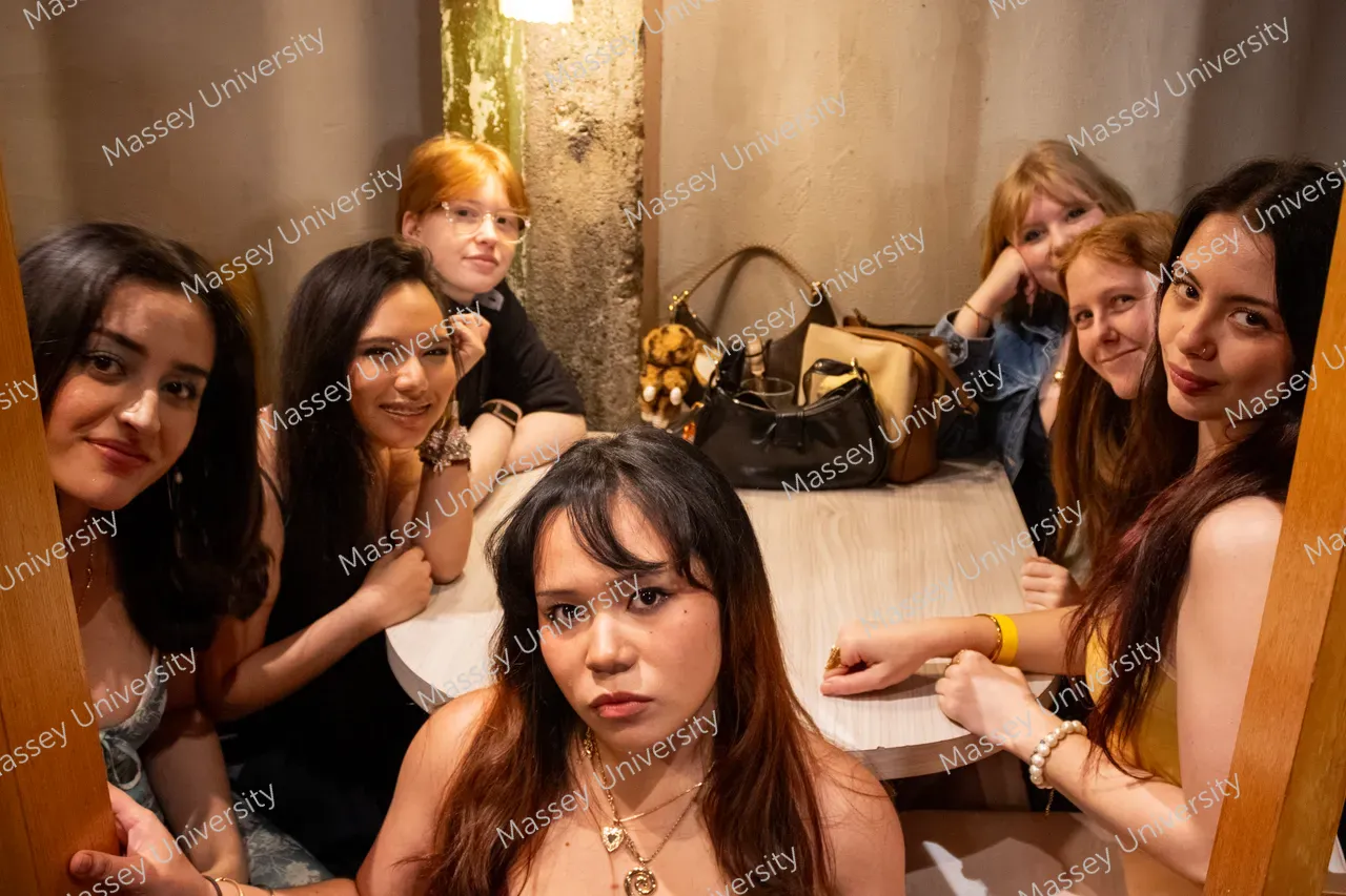 Seven young women pose around a table in a warmly lit restaurant.