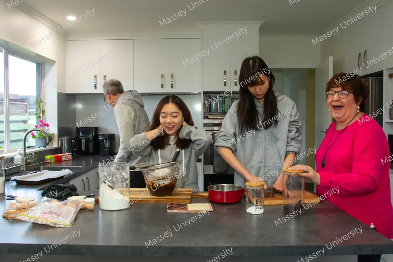 Three women and a man prepare food together at a kitchen counter.