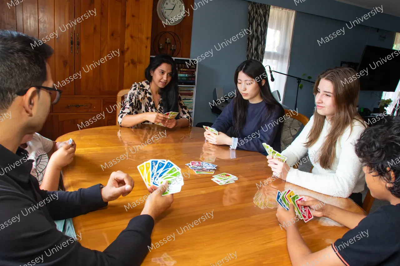 Students sit around a wooden table, holding cards during a game.