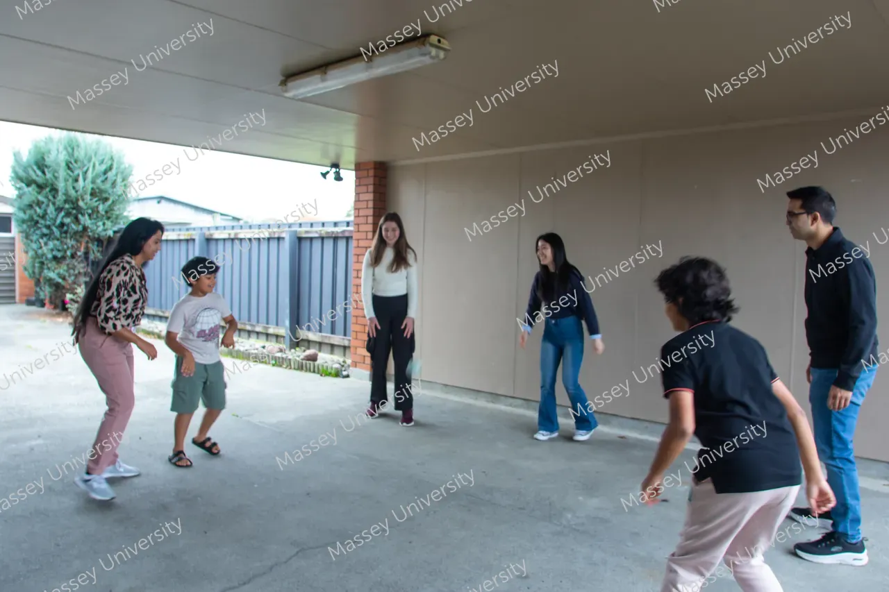 Adults and a child stand ready to play a ball game in a covered outdoor area.