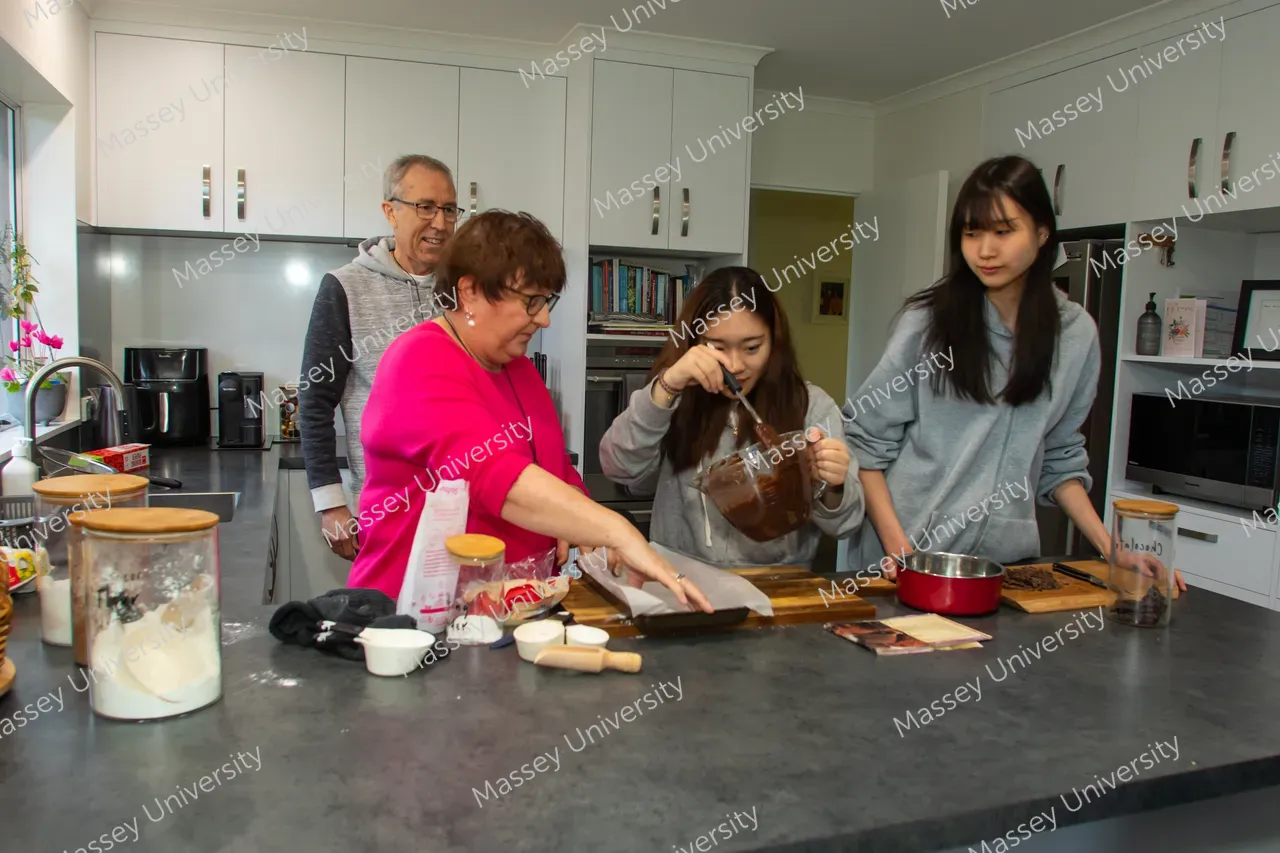 Four people prepare food together at a kitchen counter, mixing ingredients and using bowls and utensils.