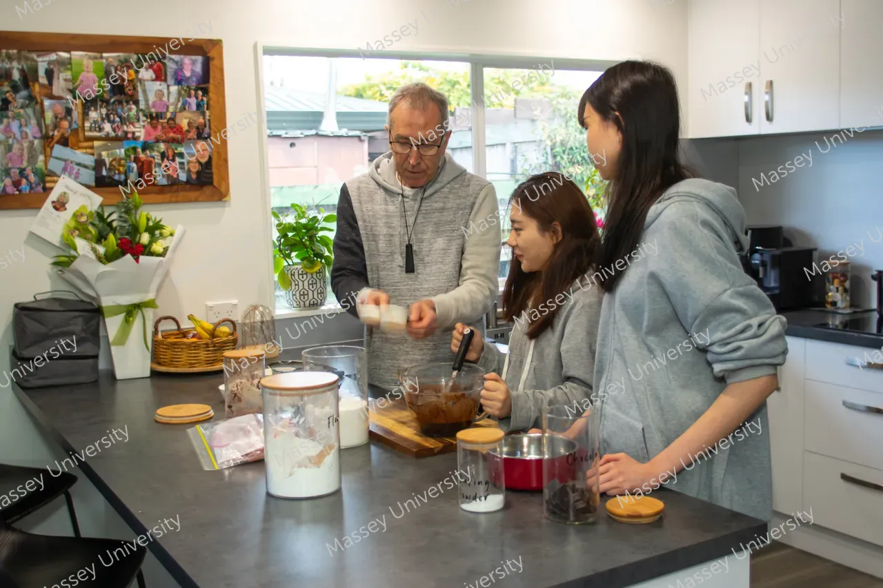 An adult and two young people mix ingredients together at a kitchen counter.
