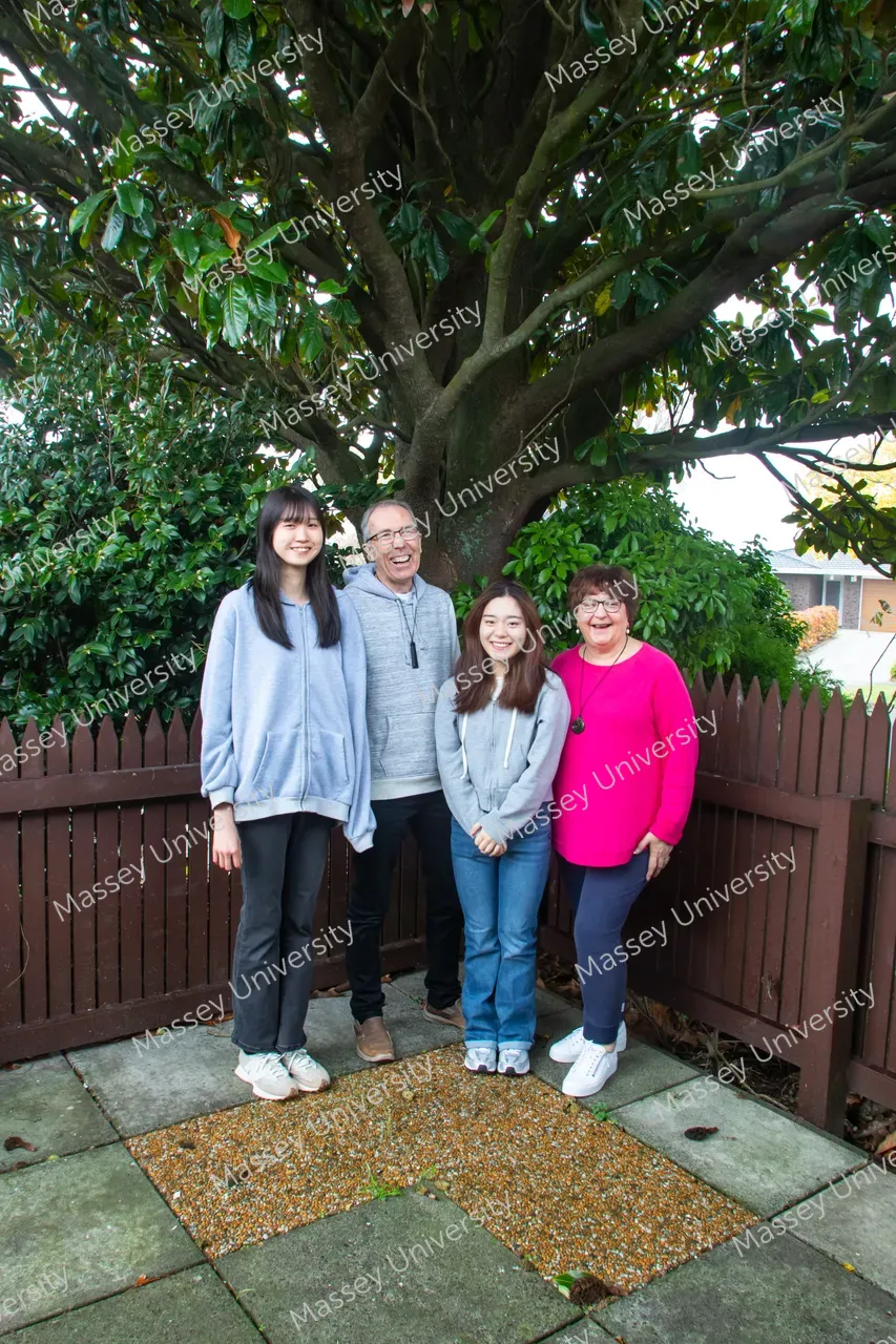 Four people pose together beneath a large tree in a garden courtyard.