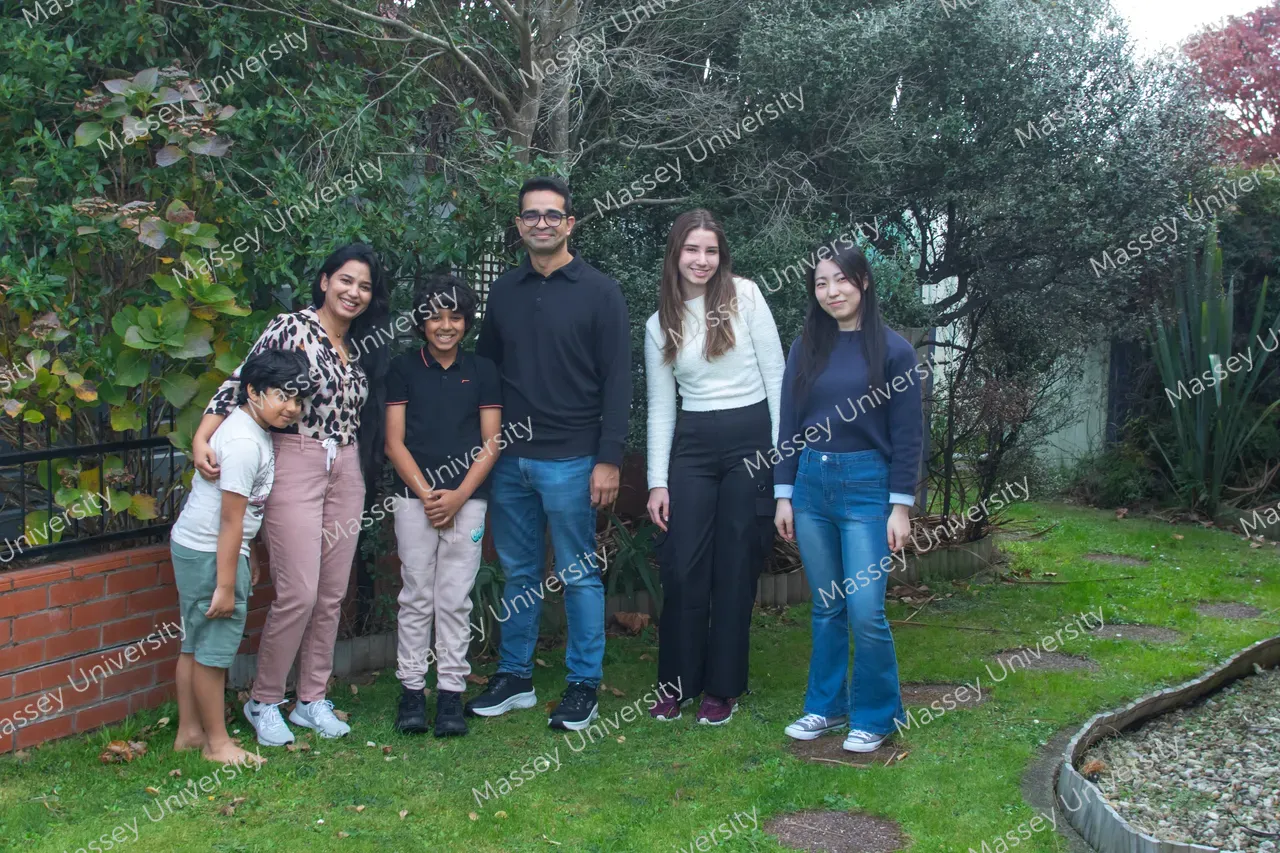 Five young people stand together on a grassy path in a garden surrounded by trees and shrubs.