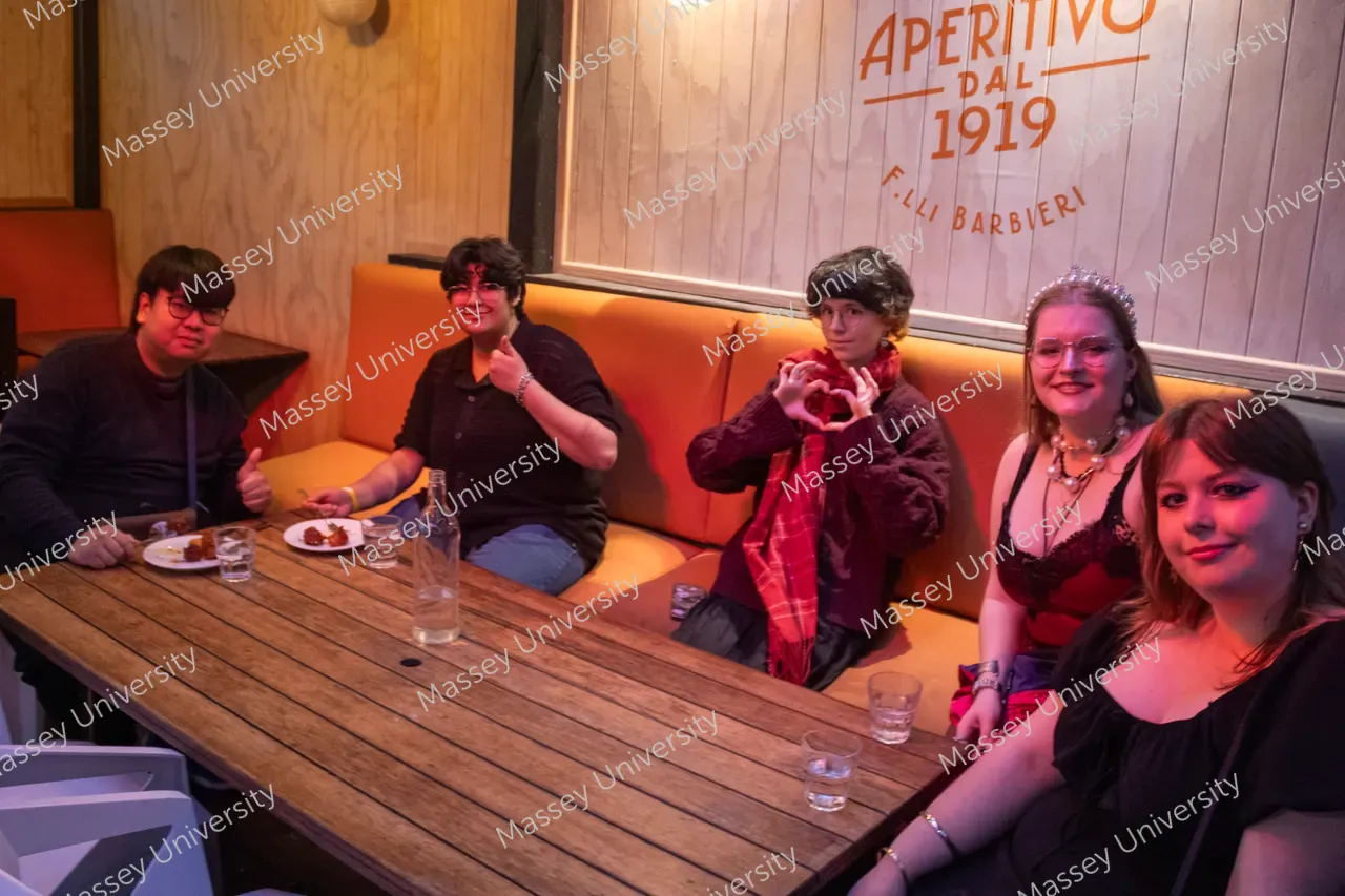 Five people pose around a wooden table in a warmly lit restaurant.