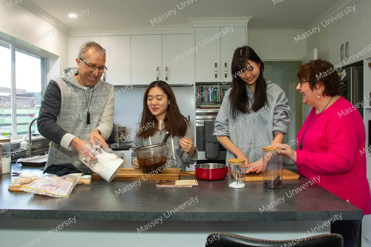 Four people prepare food together at a kitchen island, mixing ingredients in bowls and jars.