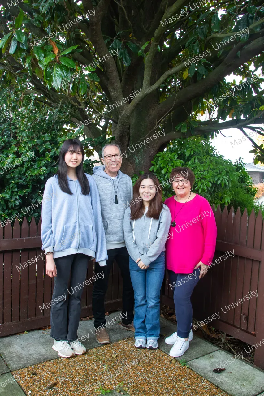 Four people pose beneath a large tree in a garden, standing in front of a wooden fence.