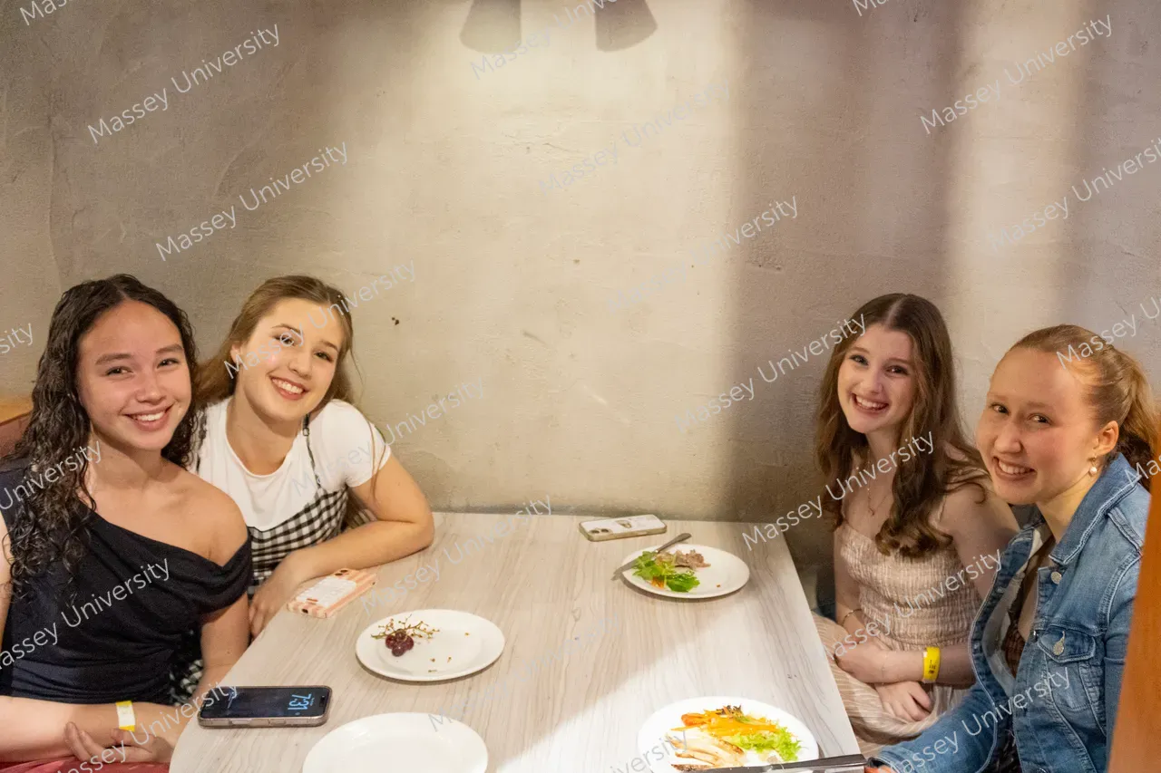 Four young women smile around a table with plates of food.