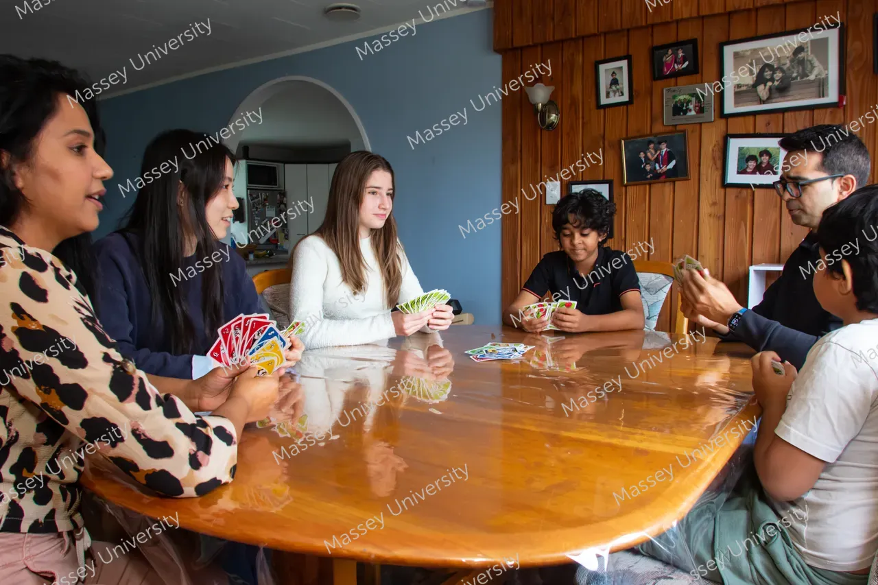 Five people sit around a wooden table playing a card game.