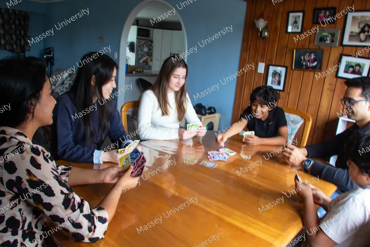 Young people sit around a wooden table, smiling and playing a card game.