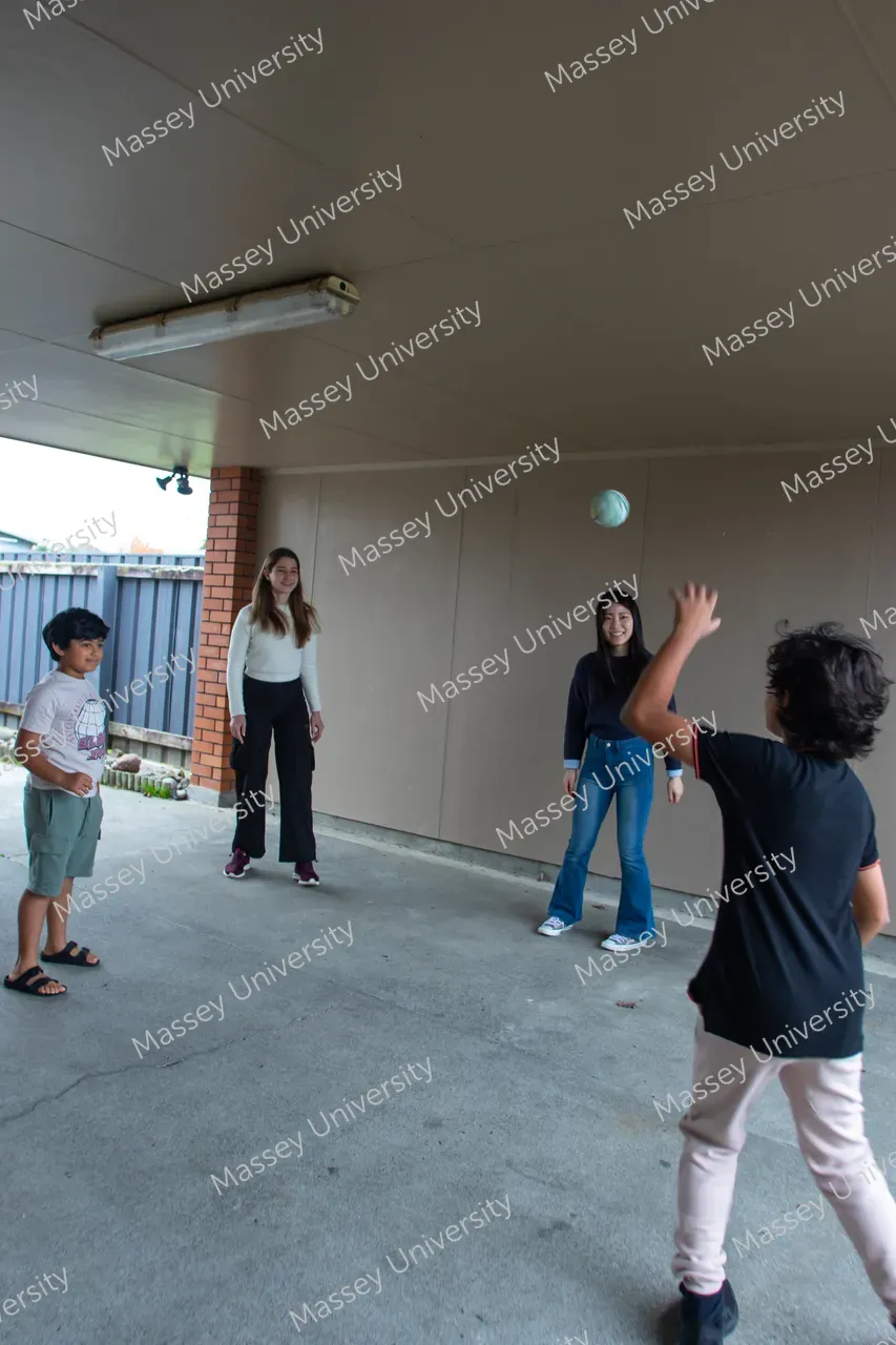 Three young people play with a ball beneath a covered outdoor area.