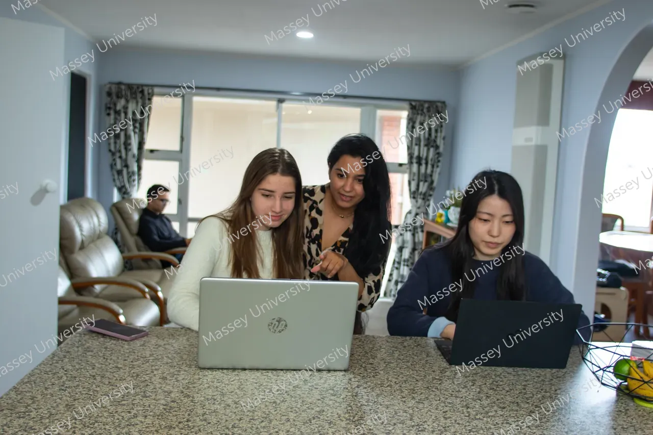 Three students work on laptops at a counter in a university lounge.