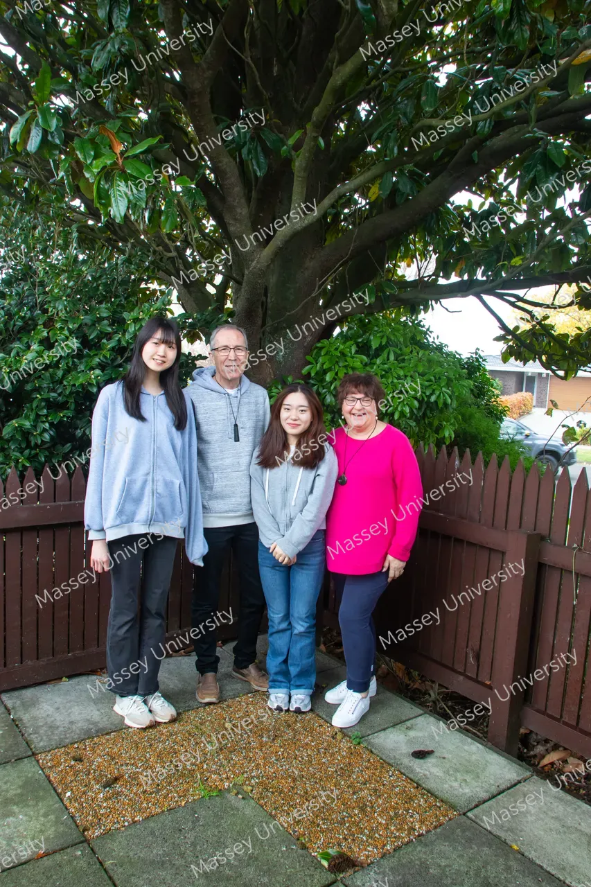 Four people pose beneath a large tree in a paved garden courtyard.