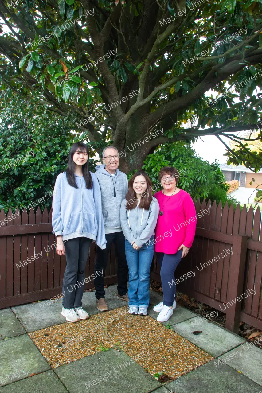 Four people stand together beneath a large tree in a garden.