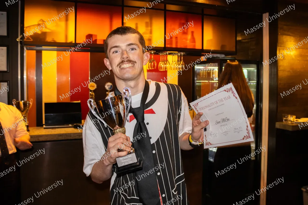 A smiling man holds a trophy and certificate inside a warmly lit bar.