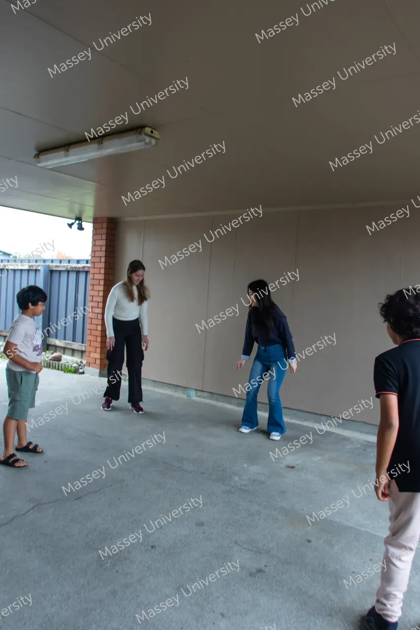 Four people stand in a covered concrete area, looking toward a small object on the ground.