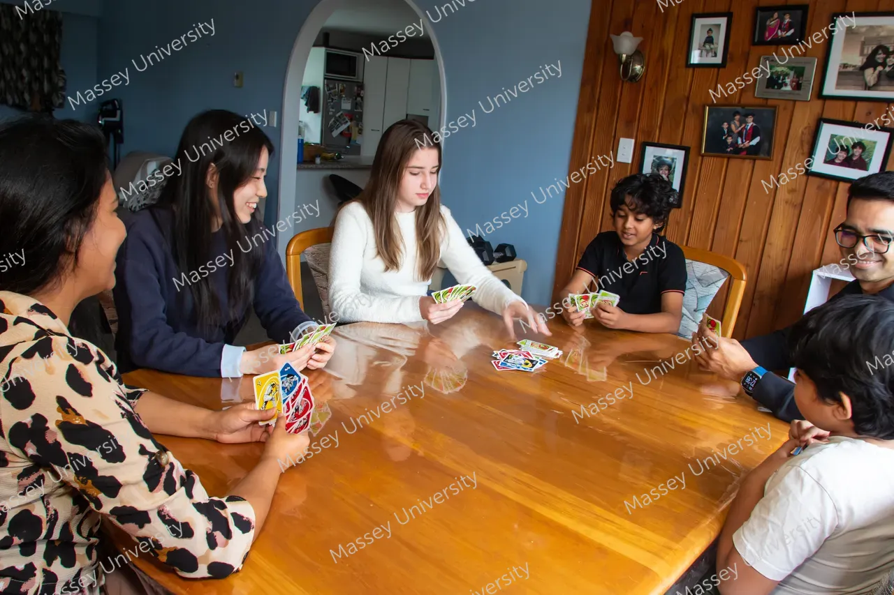 A group of young people sit around a wooden table, smiling and playing a card game.